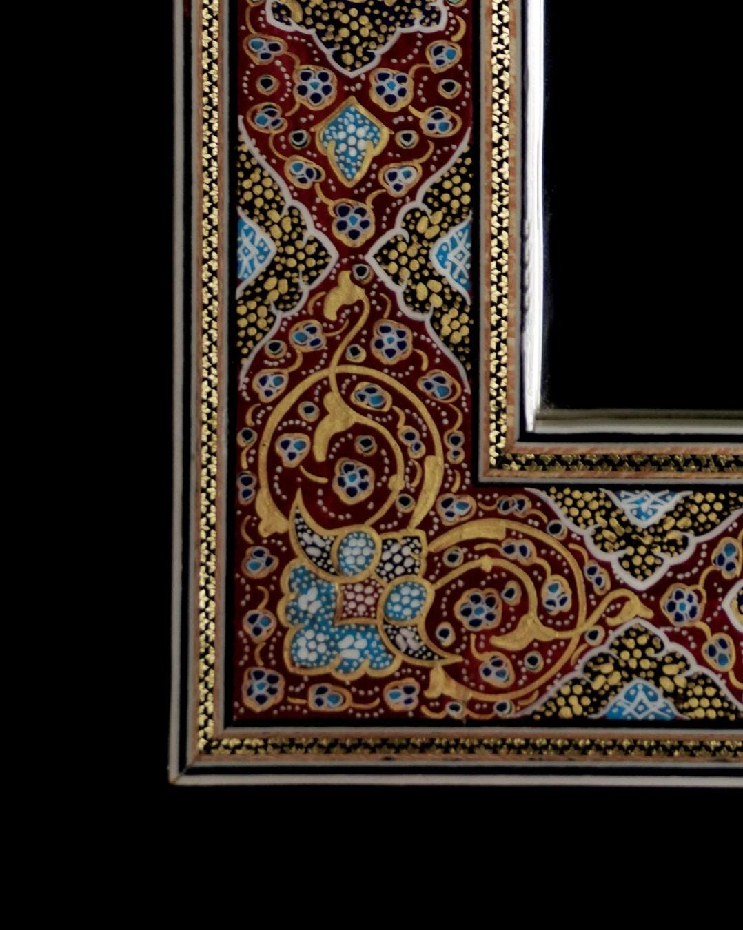 close-up of the intricate design on a hand-painted tazhib mirror frame in red, blue, and gold.