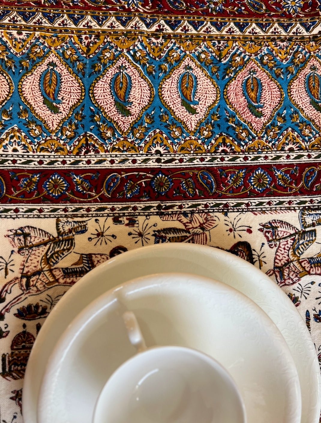 Block printed cotton textile featuring paisley motifs and horse-rider scenes with a cup and saucer.