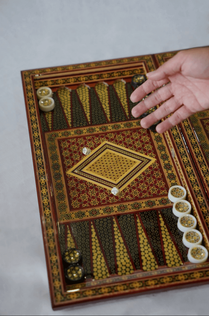Khatam inlay chess and backgammon set displayed with hand showing game pieces, showcasing intricate craftsmanship.
