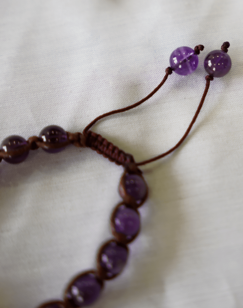 close-up of an amethyst macrame bracelet showing hand-braided natural gemstone beads and adjustable ties.