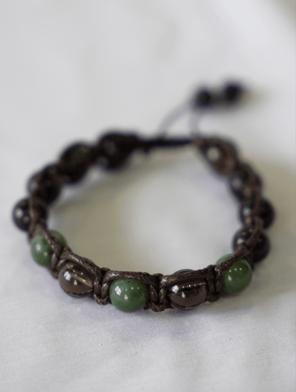 Macrame gemstone bracelet showcasing smoky quartz, jade and obsidian on a textured background.